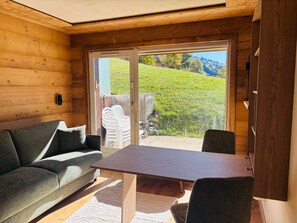 A wooden interior with a sofa, a table, and a view of a green landscape through a glass door. - Cozy apartment mountain view - 2 guests (Notre-Dame-de-Bellecombe)