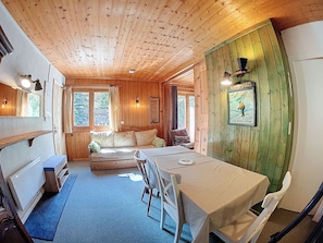 Ein Blockhaus-Interieur mit Holzbalkendecke, einem Esstisch mit Stühlen, einer Couch und einem Bett.
