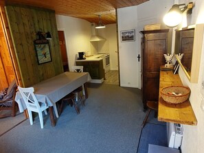 Ein gemütliches Zimmer mit Holzbalkendecke, einem Esstisch mit Stühlen, einer Küchenzeile und einem Holzkabinett mit Korb.