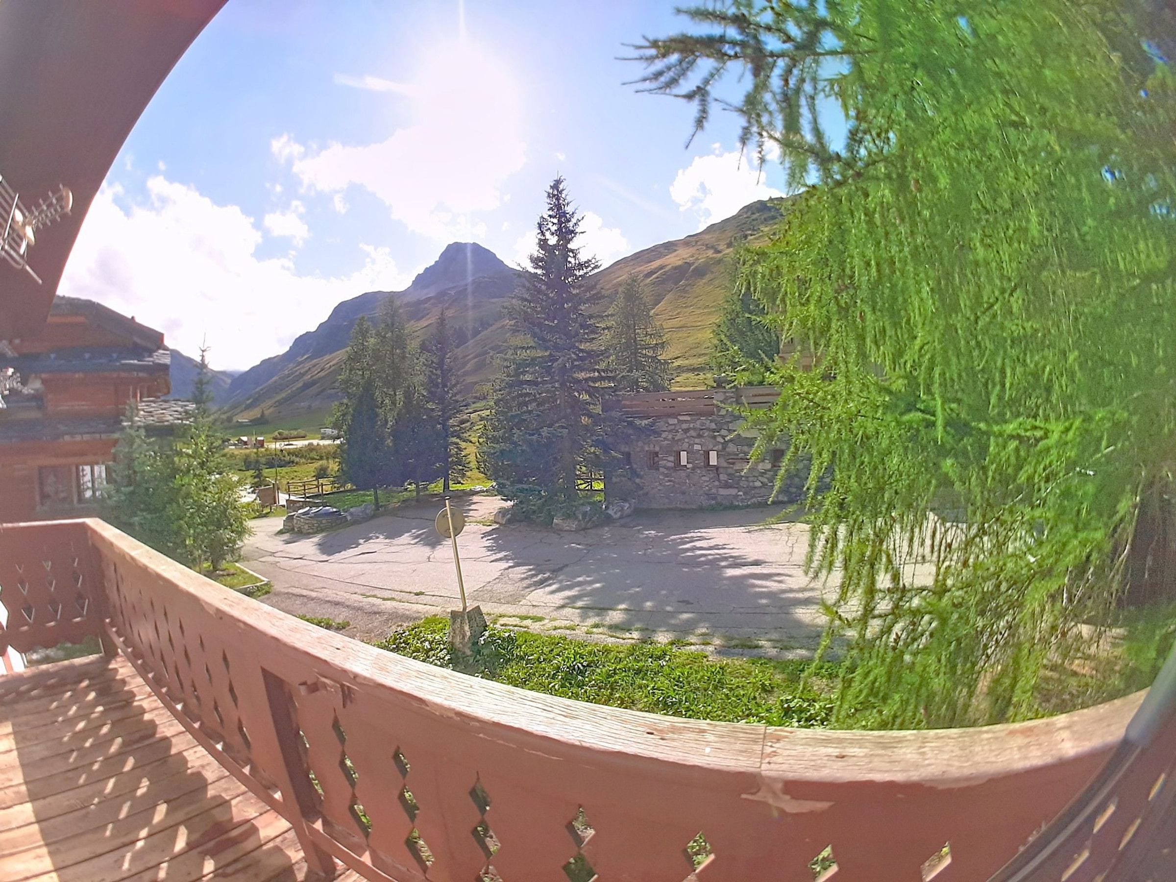 Paisaje de montaña con cielo despejado, una terraza de madera y un edificio de piedra.