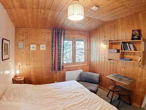 Quarto com painéis de madeira, uma cama, uma escrivaninha e uma cadeira.