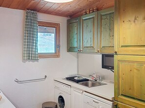 Een compacte keuken met een wasmachine, een klein spoelgedeelte en houten kastjes.