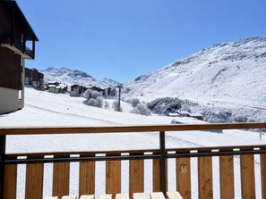 A snowy mountain landscape with buildings and a wooden balcony railing. - Luxury apartment, mountain view - 4 guests (Les Menuires)