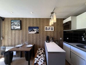 A modern kitchen with a wooden wall panel, a dining area with a bench, and a built-in oven. - Luxury apartment, mountain view - 4 guests (Les Menuires)