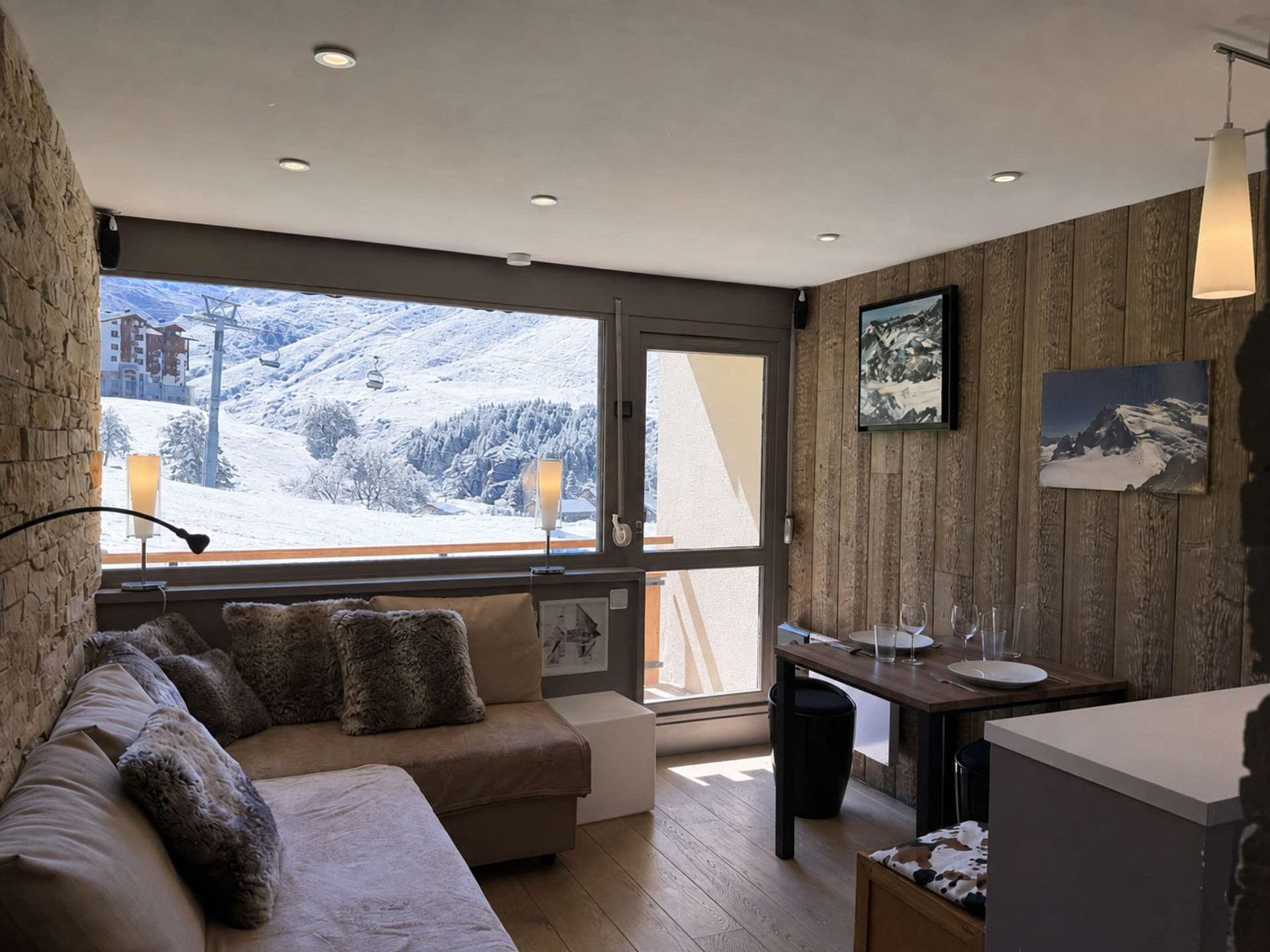 A modern living room with a sofa, a dining table, and a view of a snowy mountain landscape.