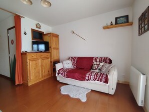 A cozy living room with a white sofa, a wooden cabinet, a television, and a radiator. - Studio near slopes - 2 guests (Crest-Voland)