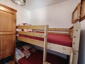 A bunk bed with a wooden headboard, a lower bunk with a red mattress, and a pillow on the floor. - Studio near slopes - 2 guests (Crest-Voland)