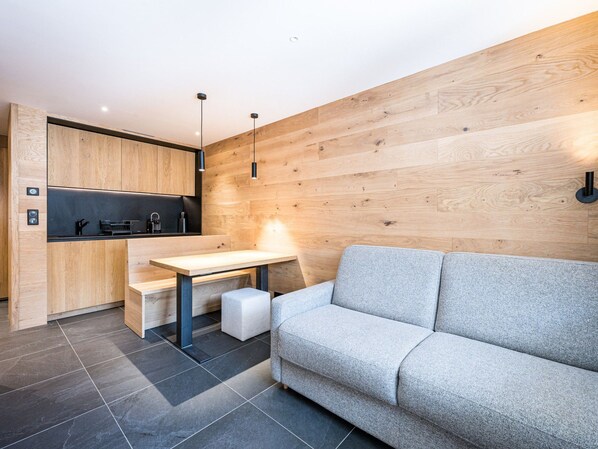 A modern kitchen with a wooden wall, a grey sofa, and a small dining table. - Renovated apartment ski-in/ski-out - 2 guests (Val-d'Isère)