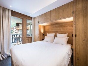 A modern bedroom with a large bed, wooden paneling, and a view of a balcony. - Renovated apartment ski-in/ski-out - 2 guests (Val-d'Isère)