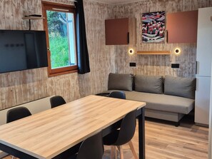 Eine moderne Küchenzeile mit eingebautem Ofen, einem Esstisch mit Stühlen, einer Couch und einem großen Fenster mit Vorhängen.