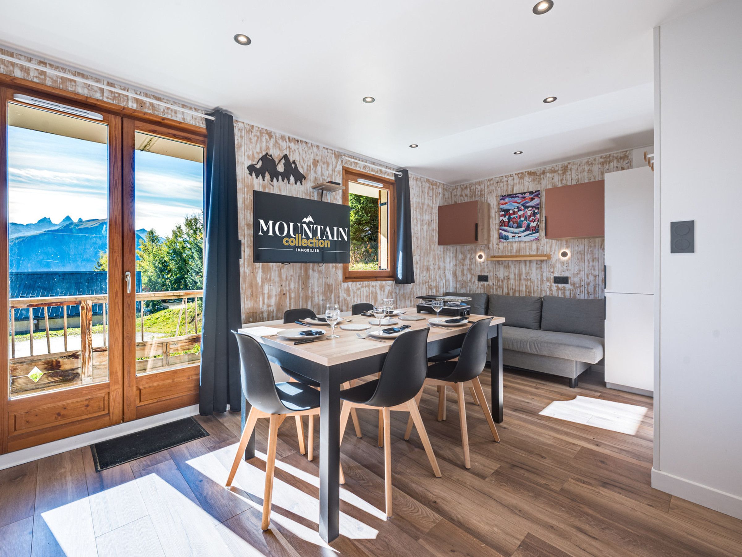 A modern interior with a dining area, a sofa, and a view of mountains.