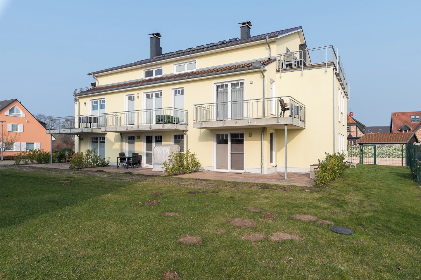 A two-story residential building with a balcony, a covered patio, and a small garden area.