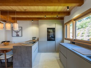 A modern kitchen with wooden beams, pendant lights, a large window, and a view of a hillside. - Half-chalet beautifully located, mountain view - 6 guests (La Clusaz)