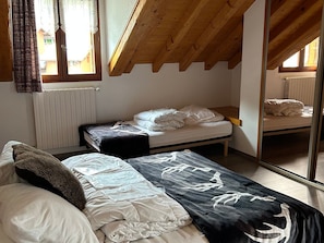 Een slaapkamer met twee bedden, een houten plafond, een raam met gordijnen en een radiator.