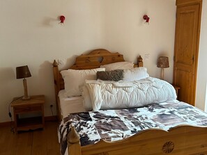 A bedroom with a wooden bed, white bedding, a nightstand with a lamp, and a wooden wardrobe. - Duplex, pets welcome - 8 guests (Valloire)