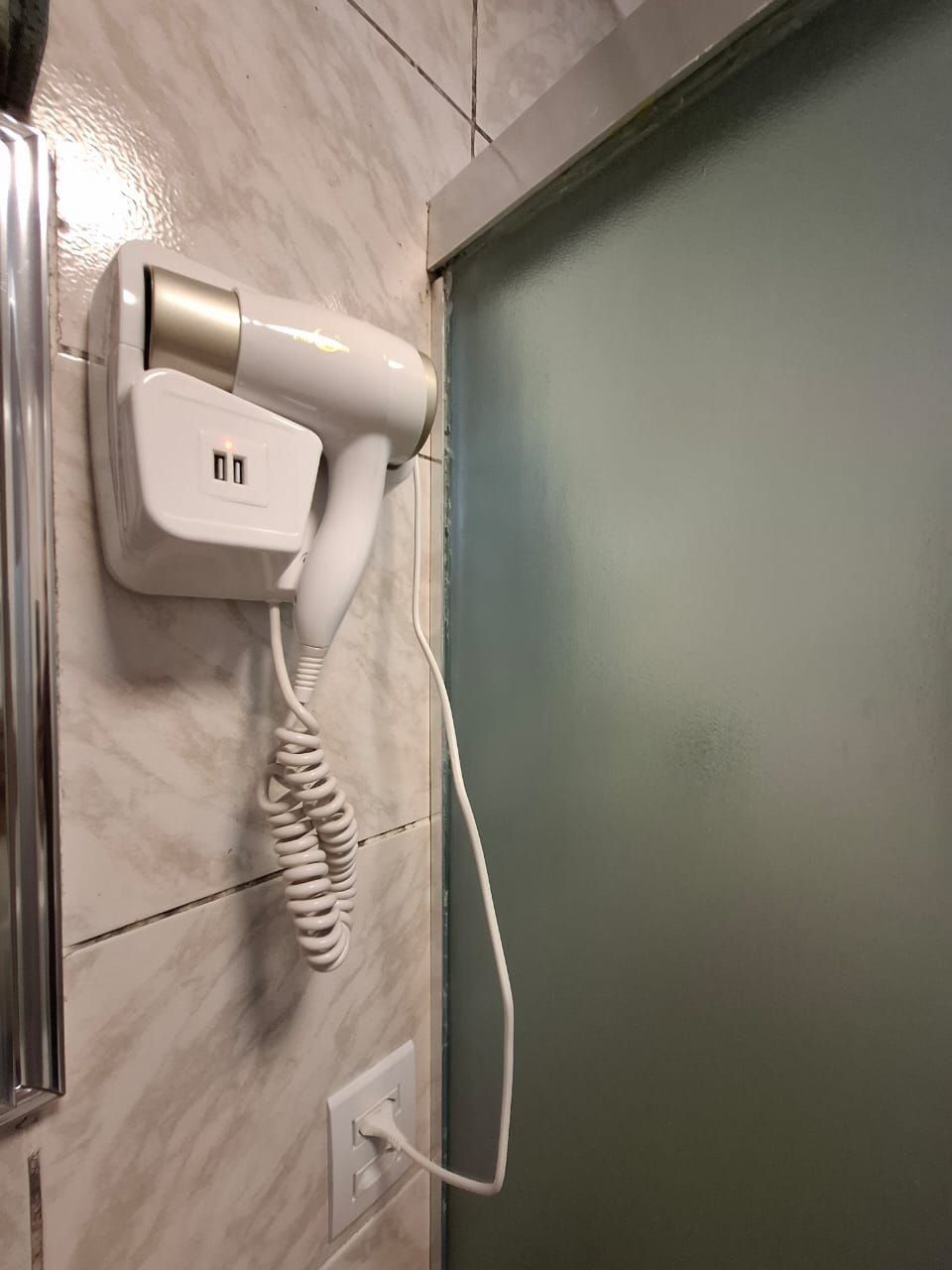 Un secador de pared con cable enchufado a una toma de corriente.