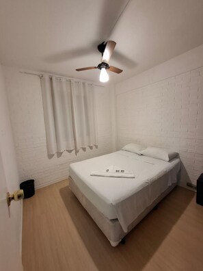 A single bed with a white mattress and pillows, a ceiling fan, and a window with white curtains. - Apartamento Vila Olímpia com 3 quartos (São Paulo)