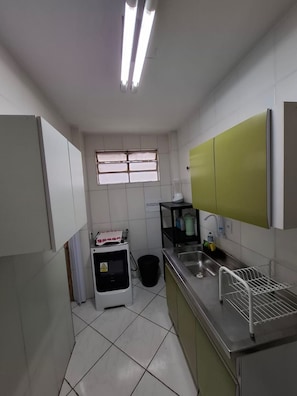A compact kitchen with white cabinets, a stainless steel sink, and a window with blinds. - Apartamento Vila Olímpia com 3 quartos (São Paulo)