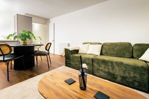 A modern living room with a green sofa, a round wooden coffee table, and a dining area with a black table and chairs. - Gorgeous 2BR Apartment in Central Chester (Cheshire West and Chester)