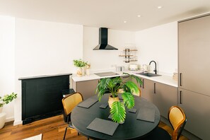 A modern kitchen with a round dining table, chairs, a black stove, and a black range hood. - Gorgeous 2BR Apartment in Central Chester (Cheshire West and Chester)