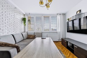 A modern living room with a white brick wall, a sofa, a coffee table, a TV, and a radiator. - Wola Central Apartment — Balcony & A/C (Warszawa)