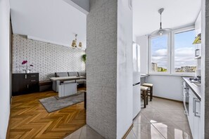 A modern kitchen with a large window, a dining area with a sofa, and a herringbone-patterned floor. - Wola Central Apartment — Balcony & A/C (Warszawa)