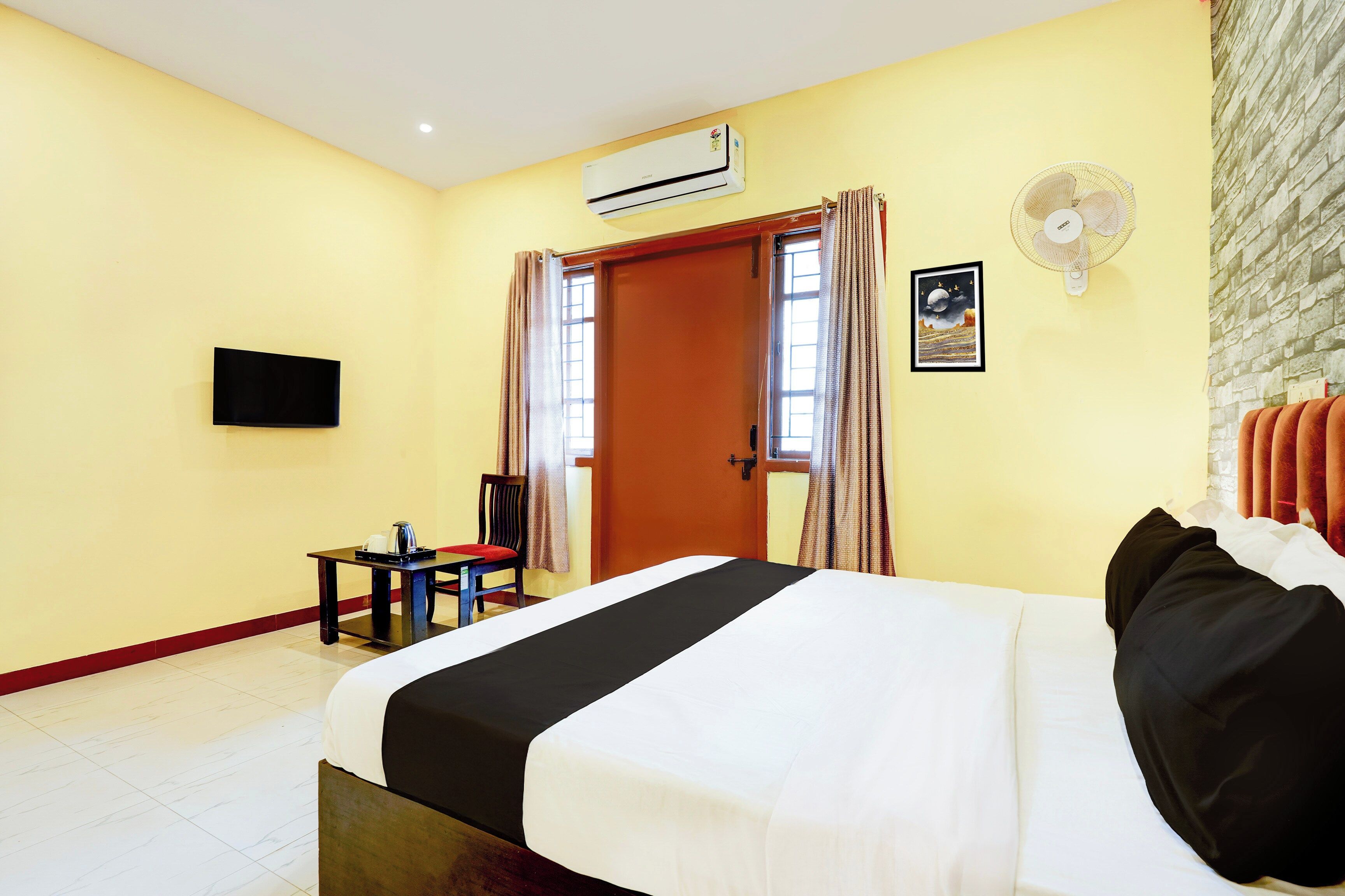 Habitación de hotel con cama, escritorio, silla, equipo de aire acondicionado, televisor montado en la pared y un marco de fotos.