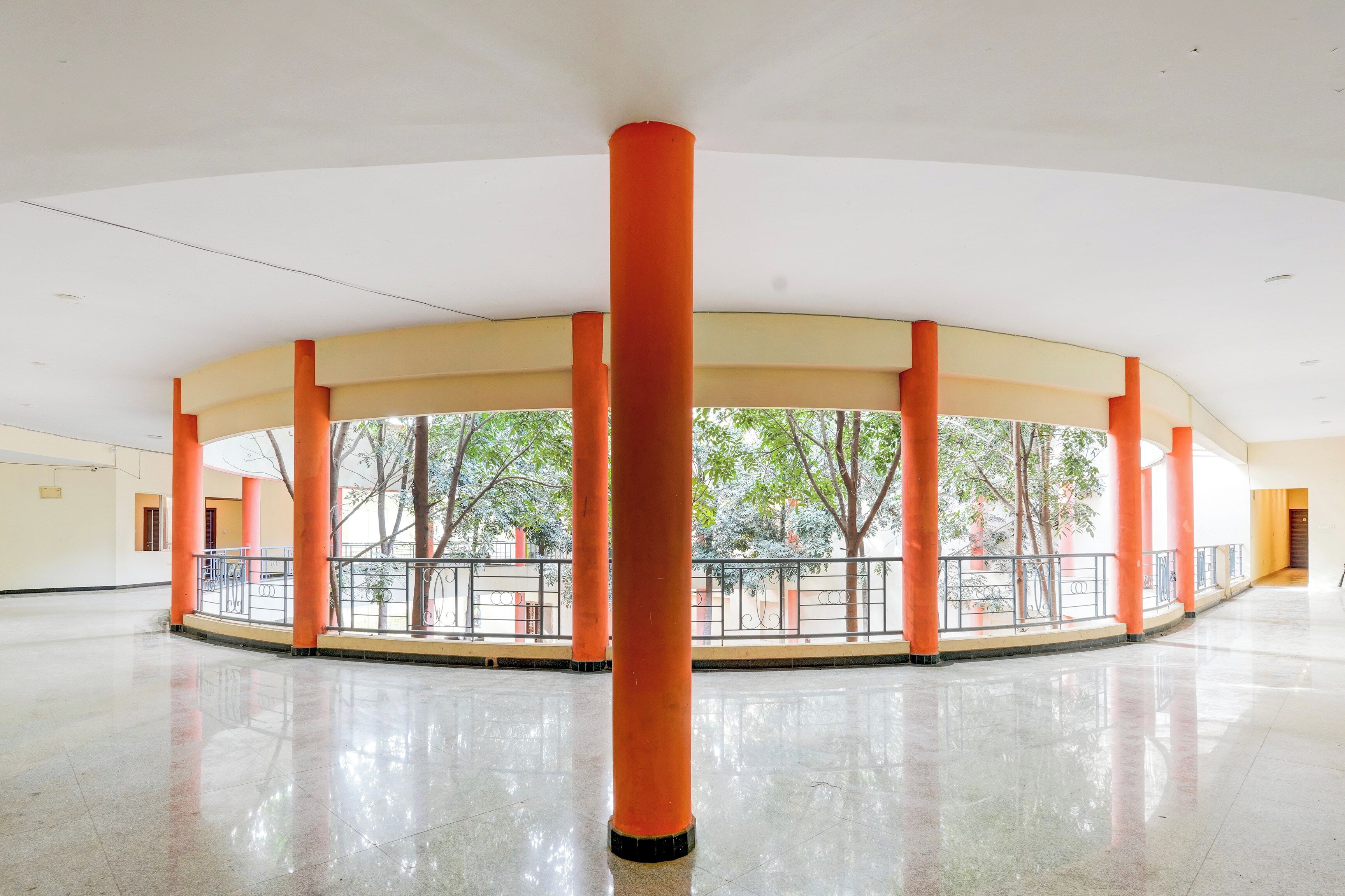 Un espacio interior amplio con techo alto, que cuenta con una columna central y una barandilla que da a un patio con árboles.