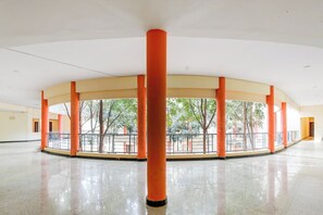 A spacious indoor area with a high ceiling, featuring a central column and a railing overlooking a courtyard with trees. - Hotel O Hennagara Rd Bommasandara (Anekal)