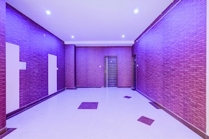 A hallway with purple brick walls, white doors, and a tiled floor. - Hotel O Hennagara Rd Bommasandara (Anekal)