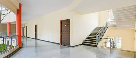A spacious corridor with a polished floor, a staircase with metal railings, and a row of doors.