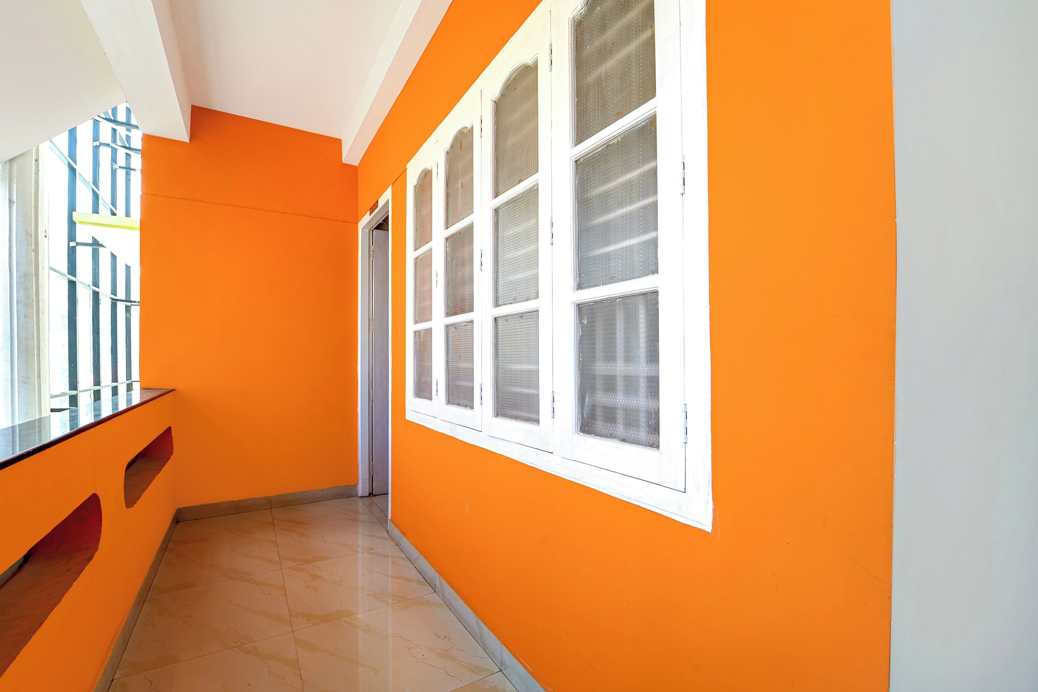 A corridor with orange walls, a white door, and a window with white frames.