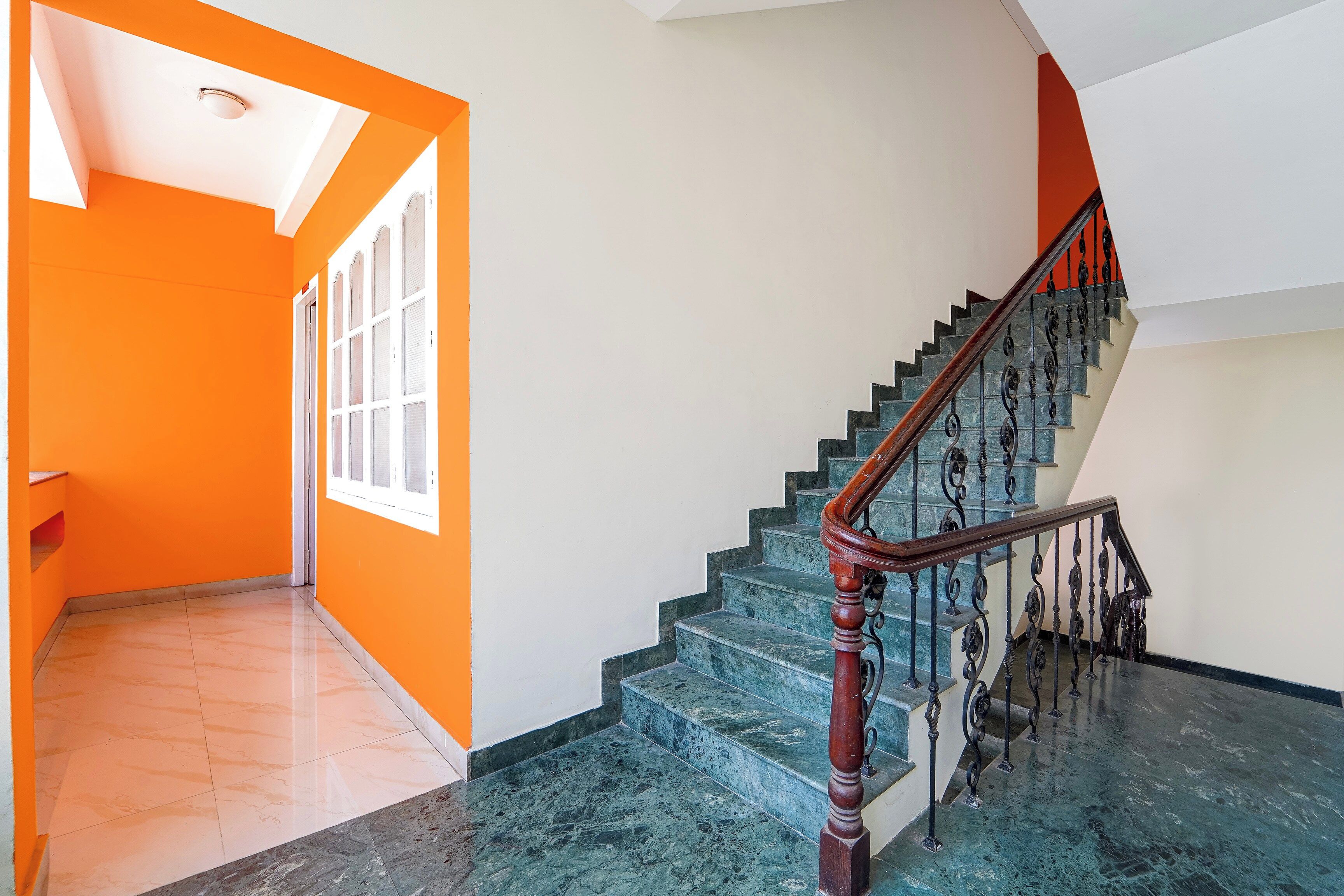 A staircase with a wooden handrail and black balusters, leading to a landing with a white door and windows.