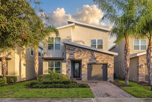 A modern two-story house with a stone facade, a front garage, and a well-maintained lawn. - 5-bedroom House in Championsgate With Private Pool (Kissimmee)