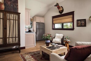 A cozy living room with a fireplace, a dining area with a table and chairs, a kitchen with a refrigerator, and a window with a view of trees. - Stardust Ranch | The Ziggy House (Fayetteville)