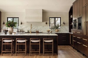 A modern kitchen with a marble countertop, dark wooden cabinets, and a central island with bar stools. - Stardust Ranch | Bowie House (Fayetteville)