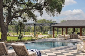 A pool area with lounge chairs, a covered seating area, and a view of a bridge in the background. - Stardust Ranch | Bowie House (Fayetteville)