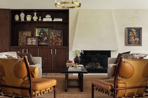 A living room with leather armchairs, a coffee table, a bookshelf with decorative items, and a fireplace. - Stardust Ranch | Bowie House (Fayetteville)