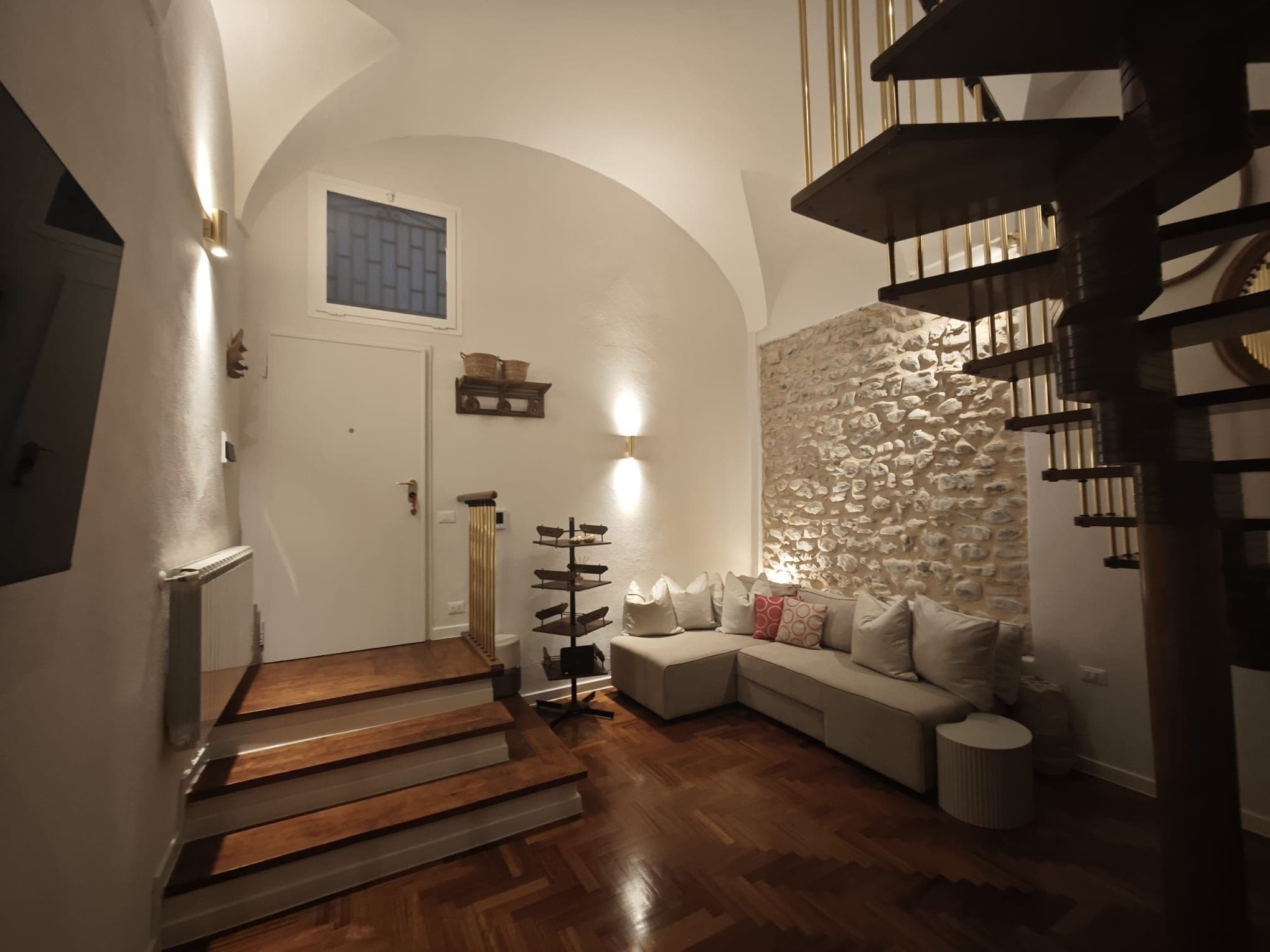 Una escalera conduce a una sala de estar con pared de piedra y un sofá.