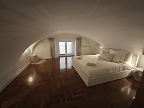 A spacious attic bedroom with a large bed, wooden flooring, and a view through a window. - Apartment 'Domus Queen Eva' with Wi-Fi and Air Conditioning (Sanremo)