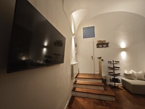 A staircase leading to a door with a small window, a wall-mounted TV, and a white sofa with cushions. - Apartment 'Domus Queen Eva' with Wi-Fi and Air Conditioning (Sanremo)