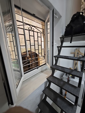 A staircase leading to a room with a barred window and a black bag on a shelf. - Apartment 'Domus Queen Eva' with Wi-Fi and Air Conditioning (Sanremo)
