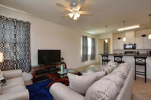 A living room with a sofa, TV, and a ceiling fan. - Disney 4BR Home w/ Pool & Lake View (Kissimmee)