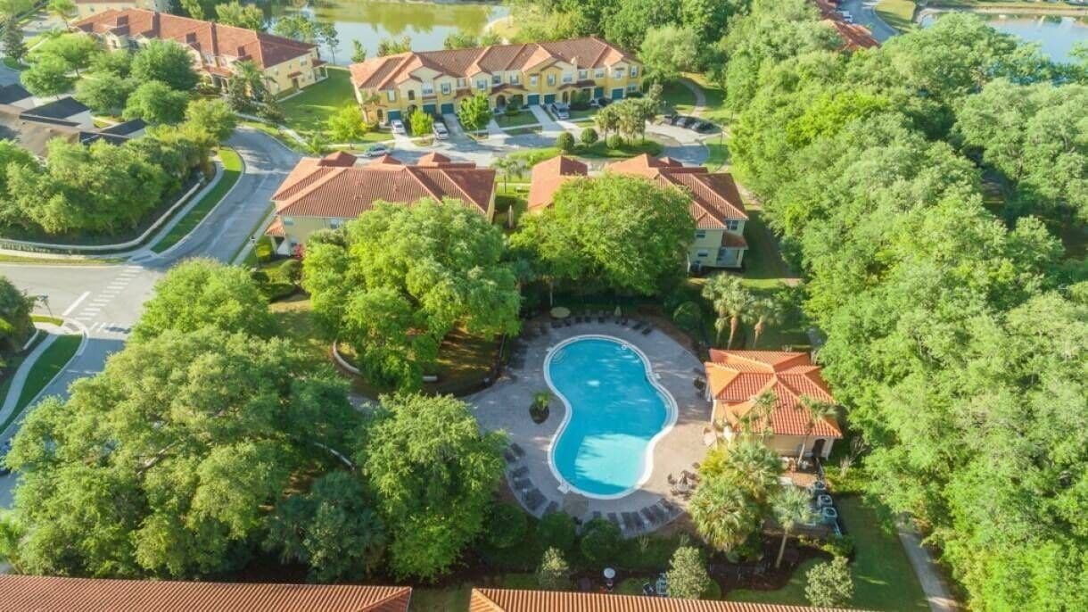 Un quartier résidentiel doté d’une piscine entourée d’arbres et de quelques bâtiments.
