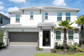 A modern two-story house with a garage, a front door, and a small garden with a palm tree. - 9br/9.5ba - 20 Guests Luxury Villa Sonoma Resort (Kissimmee)