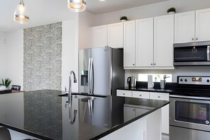 Cozinha moderna com eletrodomésticos de aço inoxidável, armários brancos e bancada de granito.