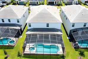 Un complexe résidentiel moderne composé de trois maisons, chacune dotée d’une grande piscine intérieure à parois vitrées.