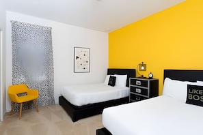 Quarto de hotel moderno com duas camas, uma mesa de cabeceira com abajur, uma cadeira pequena e um quadro na parede.