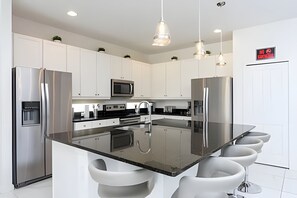 A modern kitchen with stainless steel appliances, white cabinetry, and a central island with bar stools. - 9br/9.5ba - 20 Guests Luxury Villa Sonoma Resort (Kissimmee)