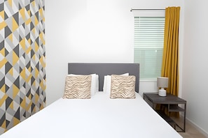 A bedroom with a bed, two patterned pillows, a bedside table with a lamp, and a window with blinds. - 9br/9.5ba - 20 Guests Luxury Villa Sonoma Resort (Kissimmee)